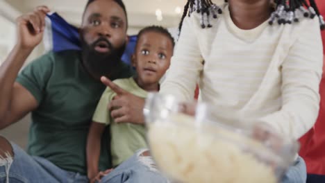 african american parents with son and daughter watching sport on tv with flag at home, slow motion