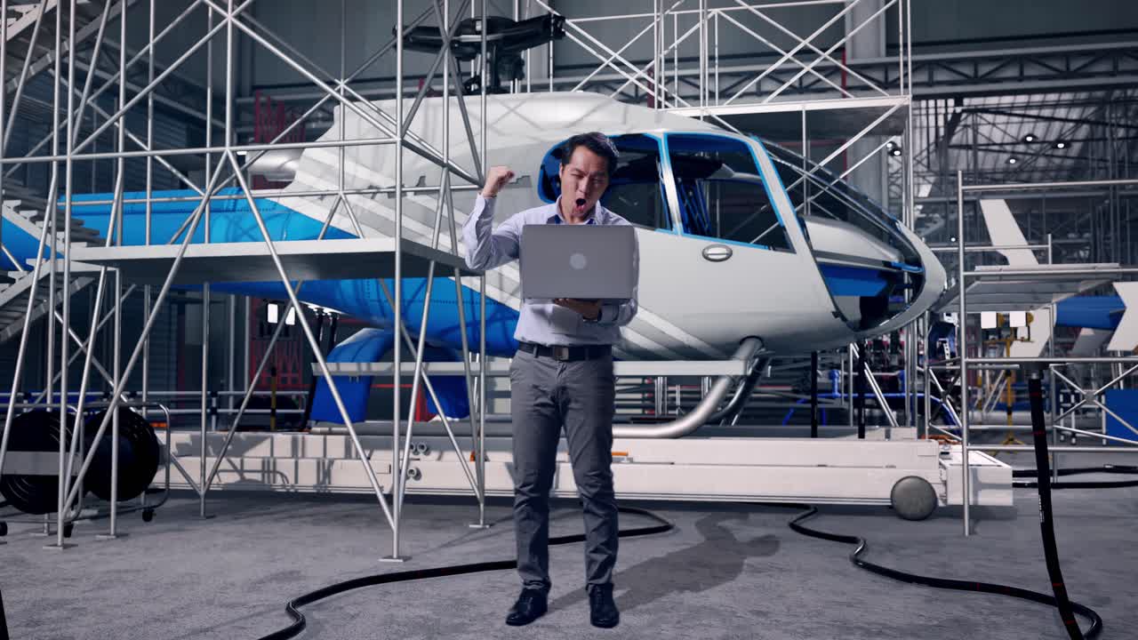 Primo piano di un professionista asiatico che ispeziona l'assemblaggio di un elicottero con il suo laptop, alza il pugno gridando "Goal"