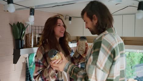 un feliz chico moreno con una camisa a cuadros verde junto con su novia morena con una camiseta a cuadros rosa eligen qué cereal preparar para el desayuno para cocinar en un remolque durante sus vacaciones en el campamento en el verano