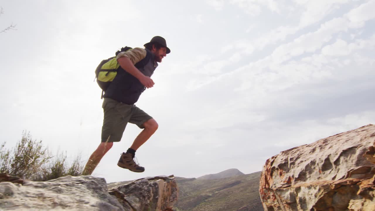 sobreviviente caucásico barbudo con mochila saltando a través de un barranco de montaña rocosa en el desierto