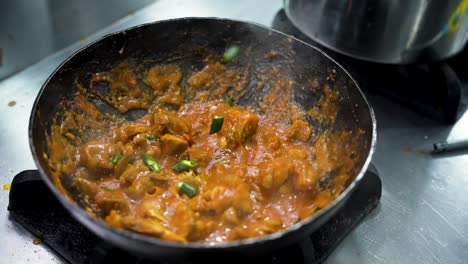 hot chicken karahi simmering as green chilies are added on top in a restaurant kitchen. pakistan