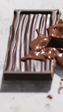 vertical video of melting chocolate being dropped on piece of chocolate bar against white background