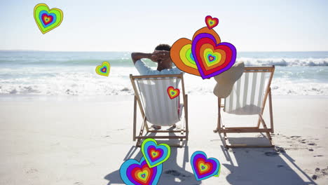 animation of hearts moving over diverse couple in love in deckchairs on beach in summer