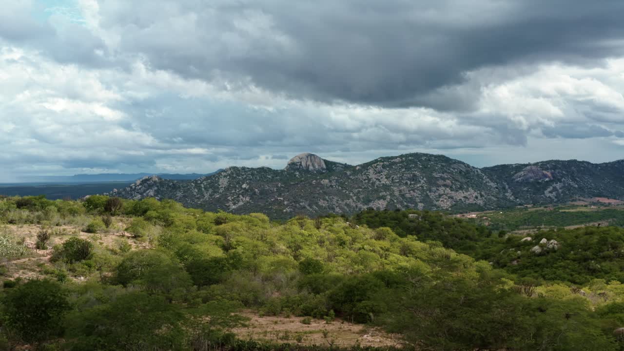 Dolly-in aerial drone extreme wide shot of the mountain range of the Pedra de Sao Pedro in Sítio Novo, Brazil in the state of Rio Grande do Norte in the countryside with rural homes and farmland
