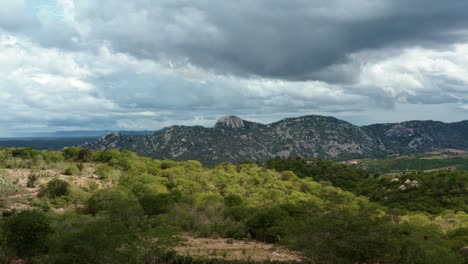 Dolly-in-aerial-drone-extreme-wide-shot-of-the-mountain-range-of-the-Pedra-de-Sao-Pedro-in-Sítio-Novo,-Brazil-in-the-state-of-Rio-Grande-do-Norte-in-the-countryside-with-rural-homes-and-farmland