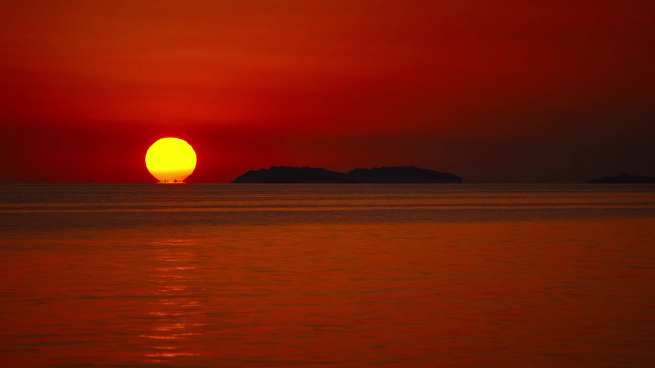 크로아티아의 지중해 해변에서 작은 파도와 함께 경치가 아름답고 자연스러운 로맨틱한 평온한 해변에서 지평선 위에 해가 지는 시간은 큰 오렌지색 공으로 지나갑니다.