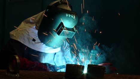 a close-up shot of a welder in full protective hse kit welding with intense light and sparks from the operation reflected on his protective mask