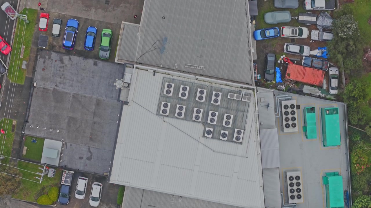 Droneoptagelse over et sikkert datacenter afslører solpaneler, kølesystemer på taget, backup-generatorer og overfyldt parkering, i skarpt dagslys i et urbant industriområde.