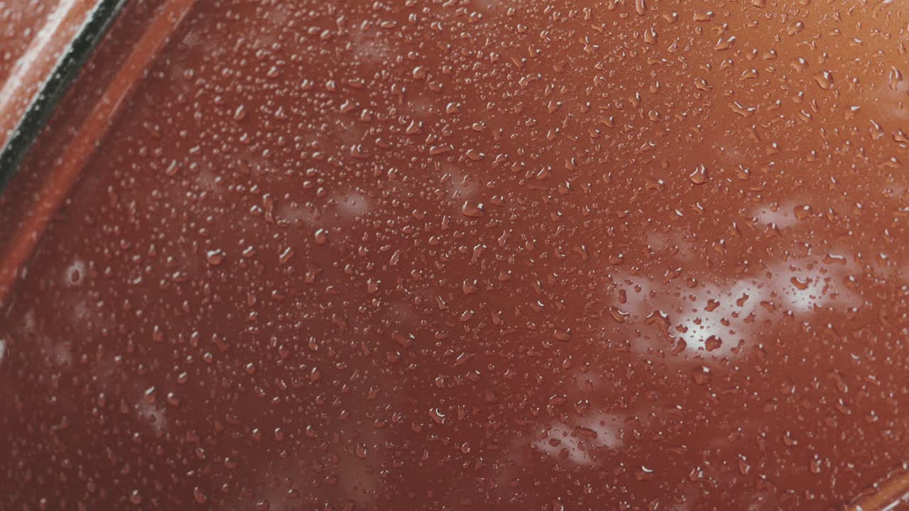 raindrops scattered on shiny orange surface of classic car
