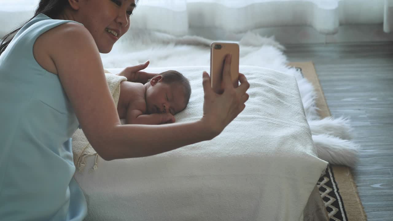 アジアの母親と新生児がスマートフォンでビデオコールで話し合っている