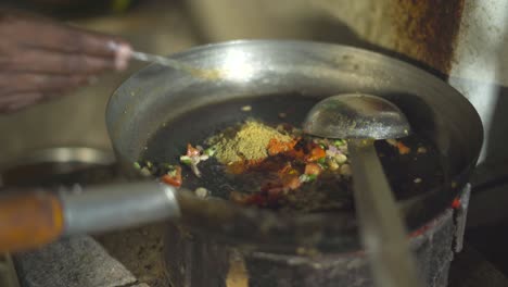 putting spices with vegetables in a frying pan for prepartion of indian meal inside kitchen of an indian dhaba or restaurant