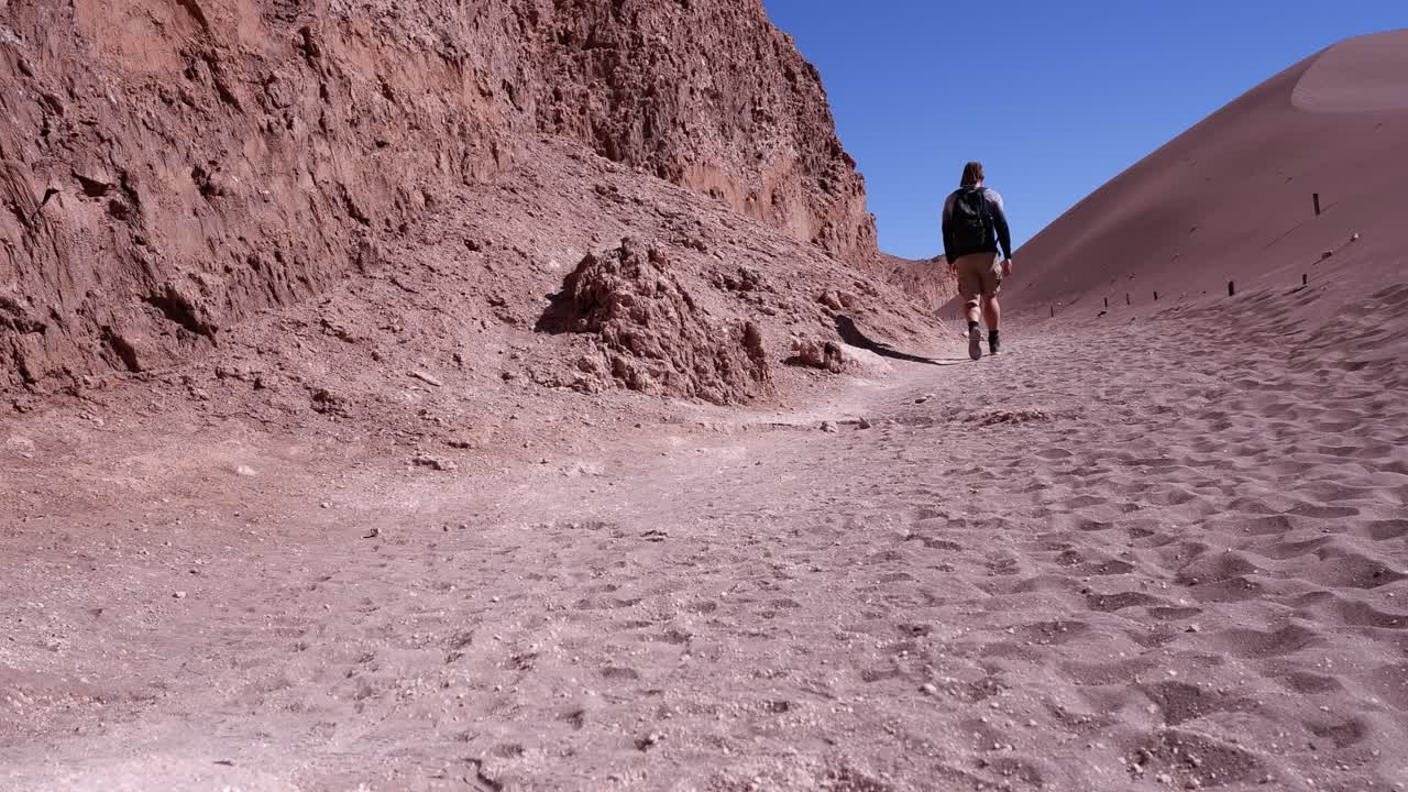 Un uomo solitario fa escursioni lungo una scogliera rocciosa nel deserto di sabbia rossa, regione di Atacama, Cile