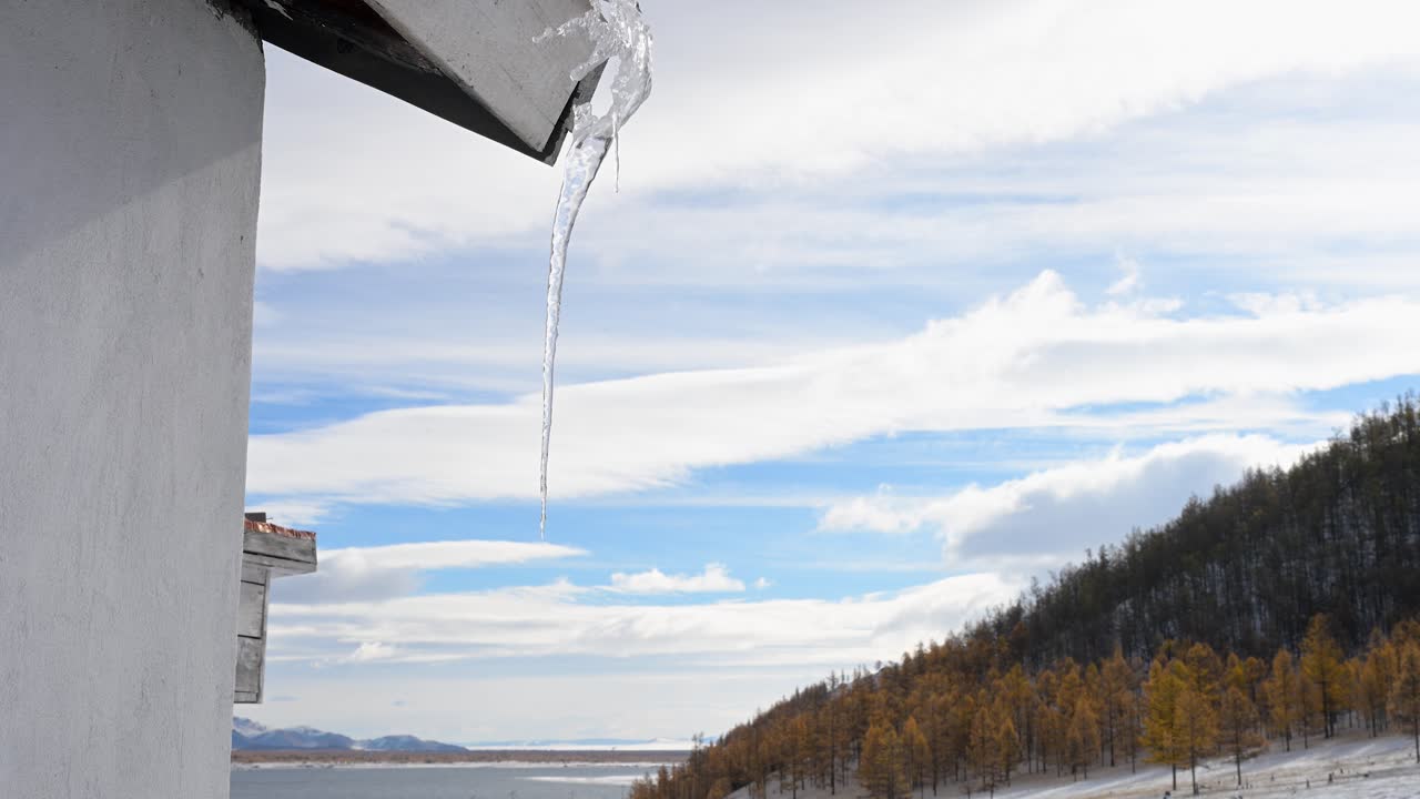 An icicle hangs from the roof of a rustic log cabin in a remote Mongolian forest. A peaceful scene of winter solitude and life in a cold, natural environment