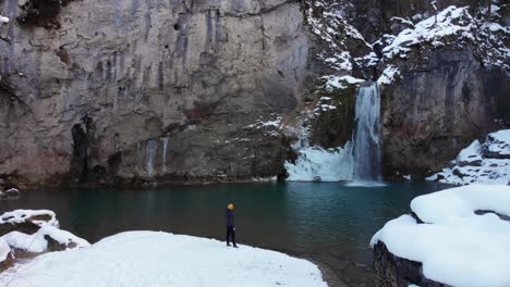 hombre caminando hacia la cascada en temporada de nieve, dron avanzando desde el aire y acercándose a la cascada