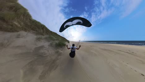a person paraglides over sand dunes on a sunny day at the beach near the ocean