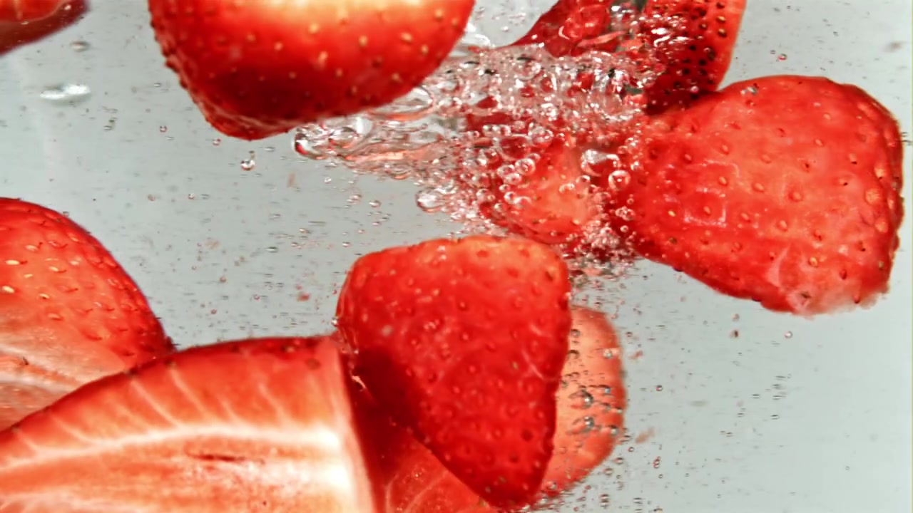 Fette di fragola rossa fresca che galleggiano in acqua frizzante.