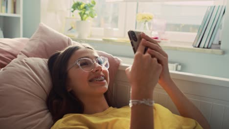 Caucasian-teenage-girl-having-video-call-while-lying-on-back-in-her-bed