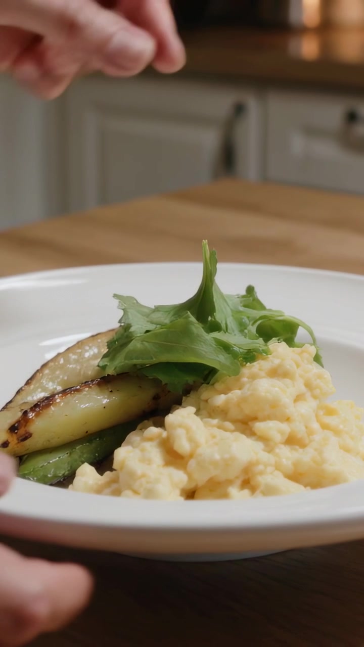 Video verticale: Mano di chef con manica che entra in scena, posizionando una foglia su uova e fette sul bancone.
