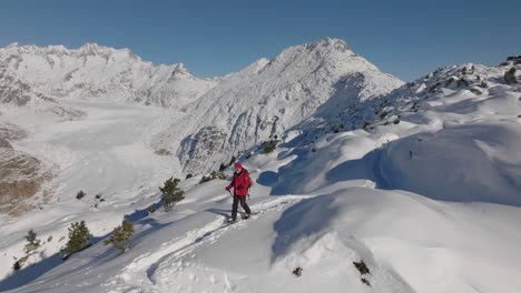 aerial shot in switzerland with a person walking with snow shoes on a sunny day with a glacier behind