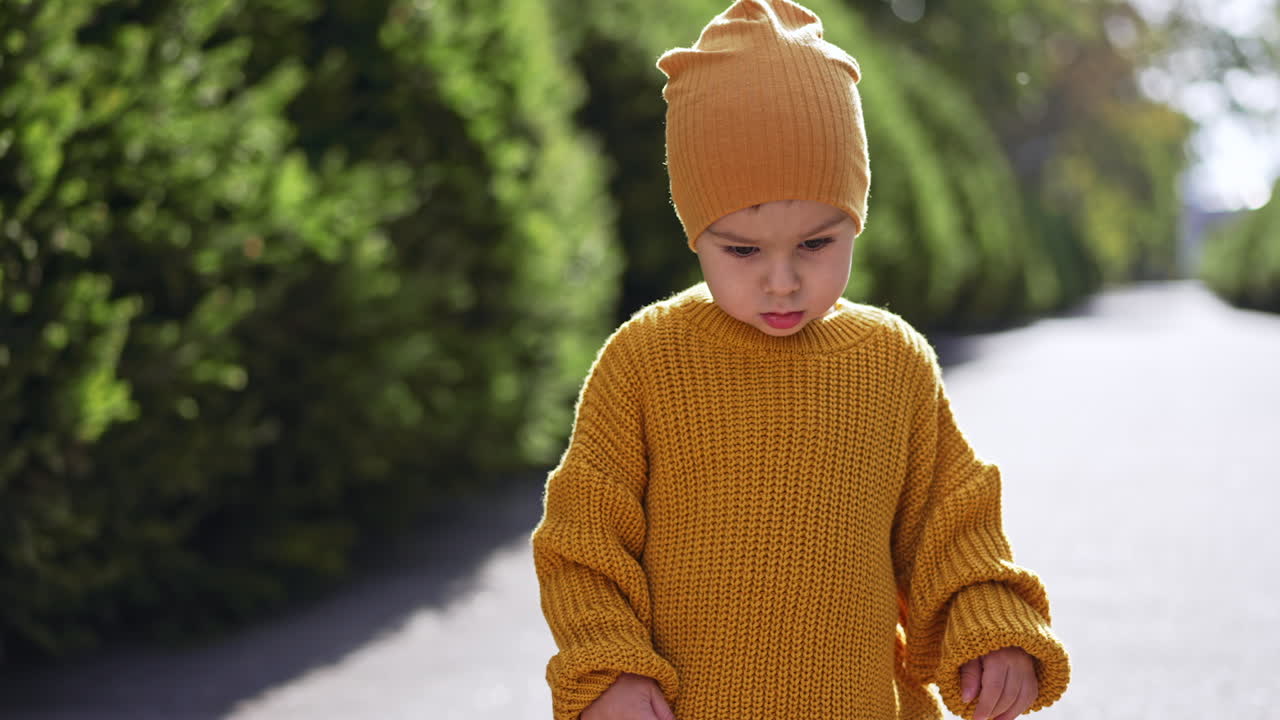 Caucasian toddler wearing yellow cap and knitted sweater. Baby boy is outdoors on sunny weather. Blurred backdrop.