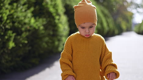 caucasian toddler wearing yellow cap and knitted sweater. baby boy is outdoors on sunny weather. blurred backdrop.