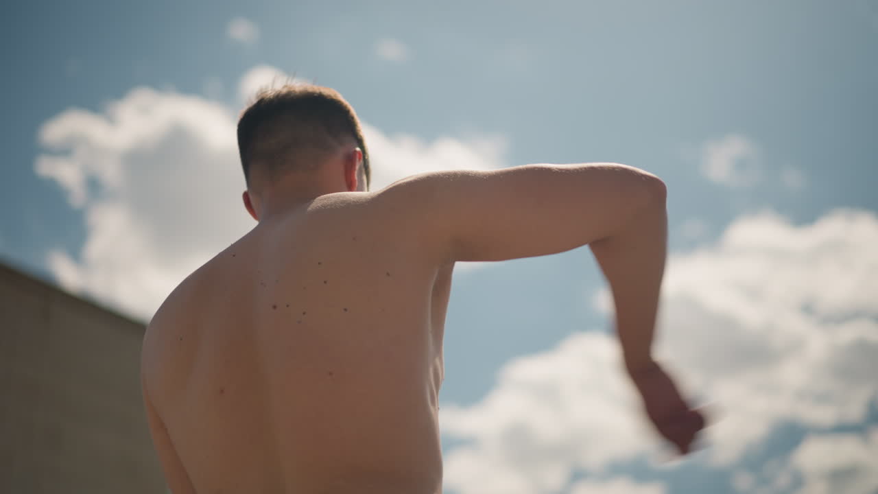 hombre refrescándose, momento de calma con luz solar y sombras suaves, escena tranquila de un hombre refrescándose bajo el cielo abierto, imagen serena de un individuo sin camiseta haciendo una pausa para secarse la cara bajo la luz del día brillante