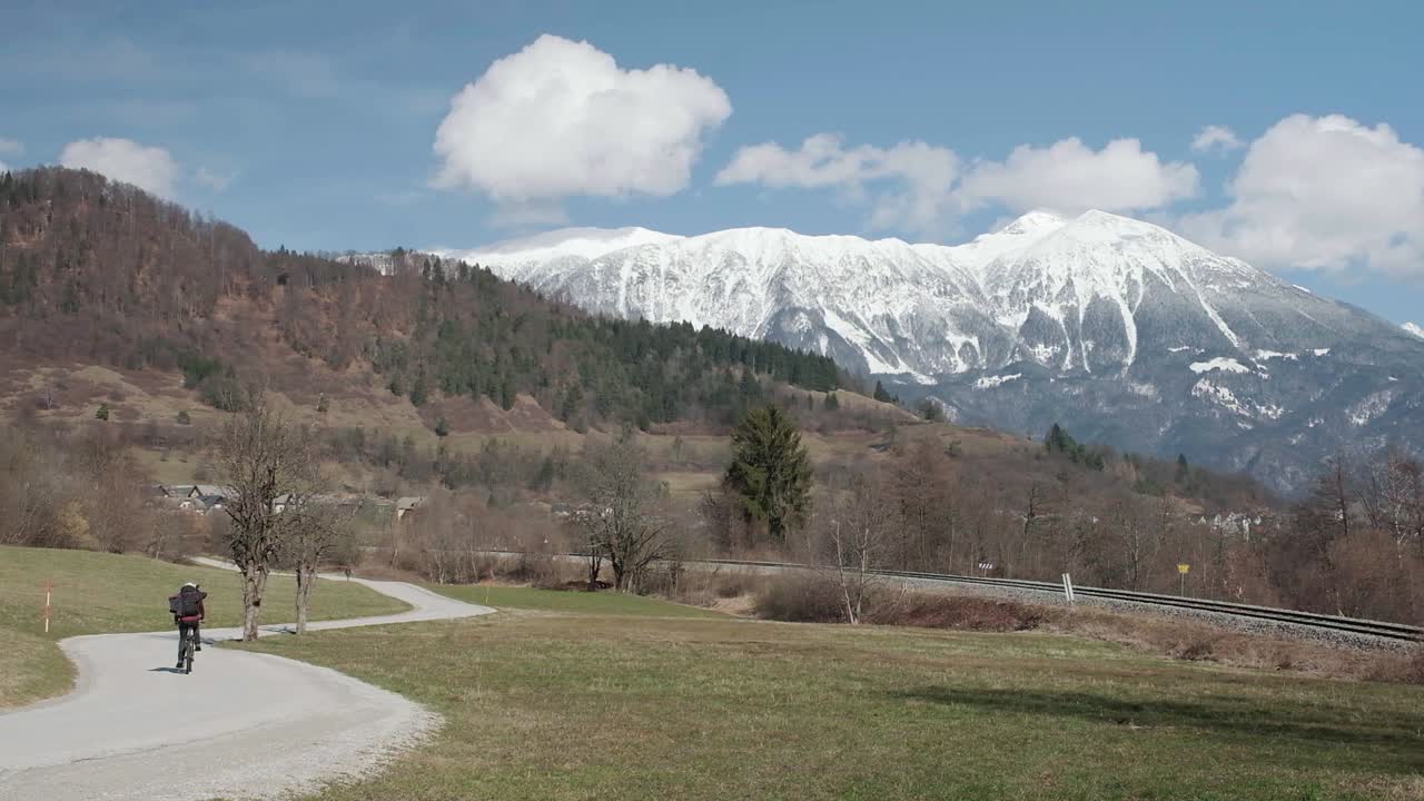 andar en bicicleta lejos de la cámara en invierno por un camino ventoso en eslovenia con la montaña stol en el fondo