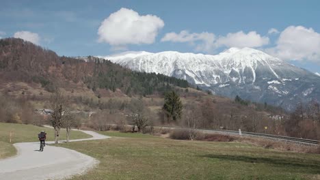 andar en bicicleta lejos de la cámara en invierno por un camino ventoso en eslovenia con la montaña stol en el fondo