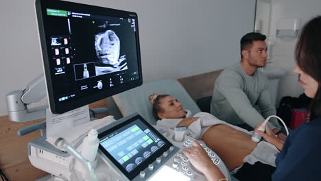 sonography examination of a pregnant lady. doctor sits at the equipment pressing on the machine buttons.