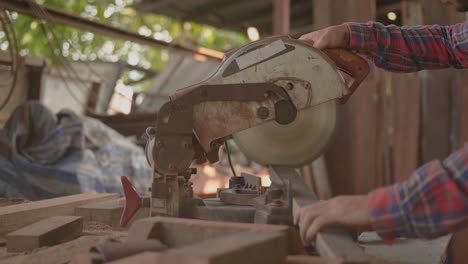 close up of handsome carpenter man wearing goggles and earmuffs for personal safety using circular saw cut wood for furniture in workplace.