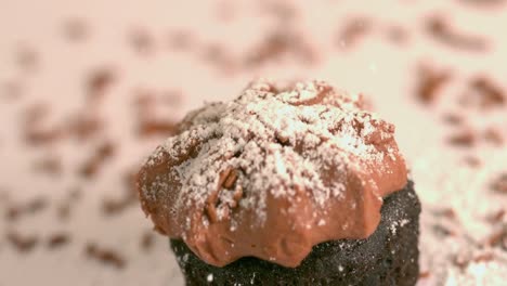 icing sugar being sieved on chocolate frosted cupcake