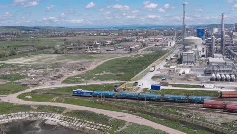 a wide aerial drone shot pans to follow a freight train moving through the azomures chemical factory. the vast industrial landscape includes smokestacks, silos, and a rail yard