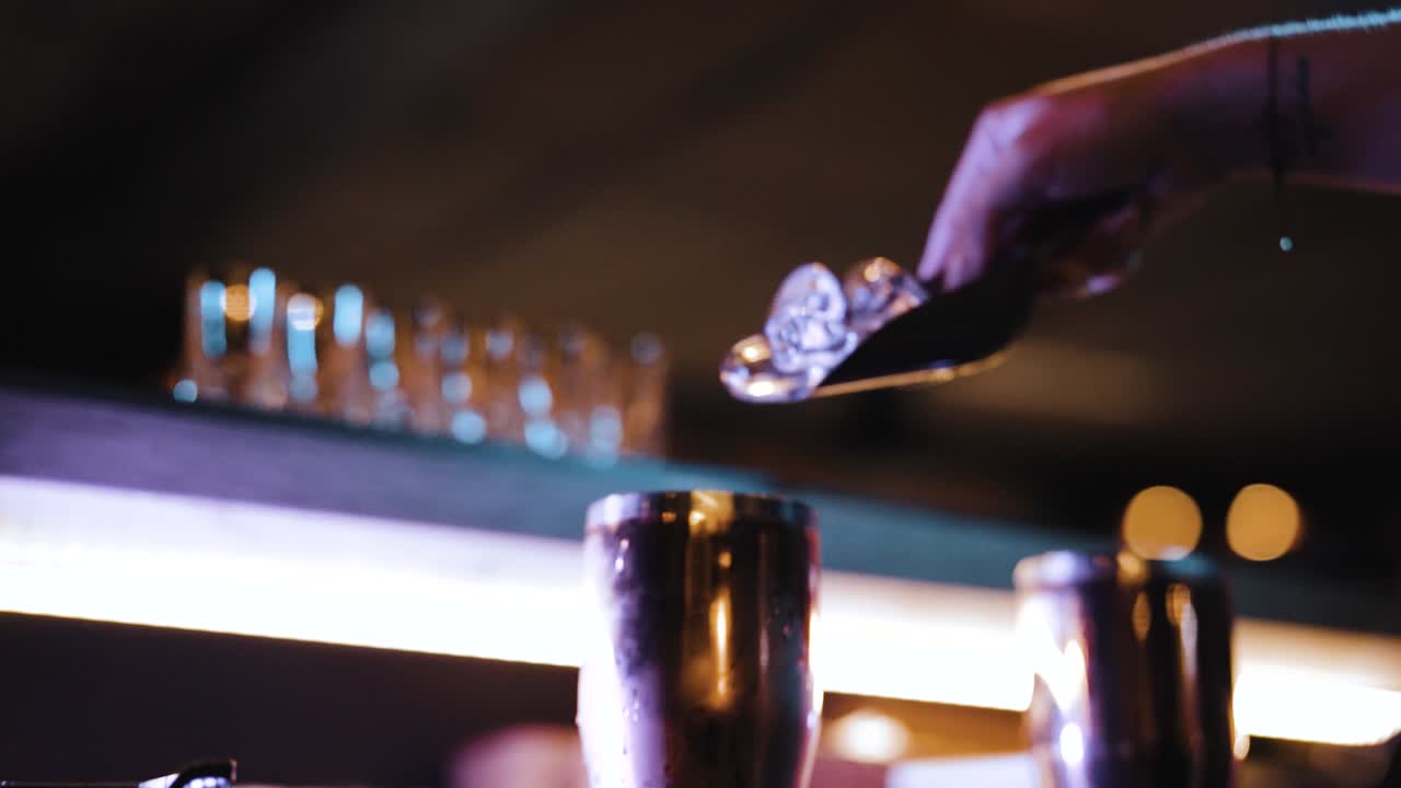 tattooed bartender's hand adding ice cubes to bar shaker (slow motion)