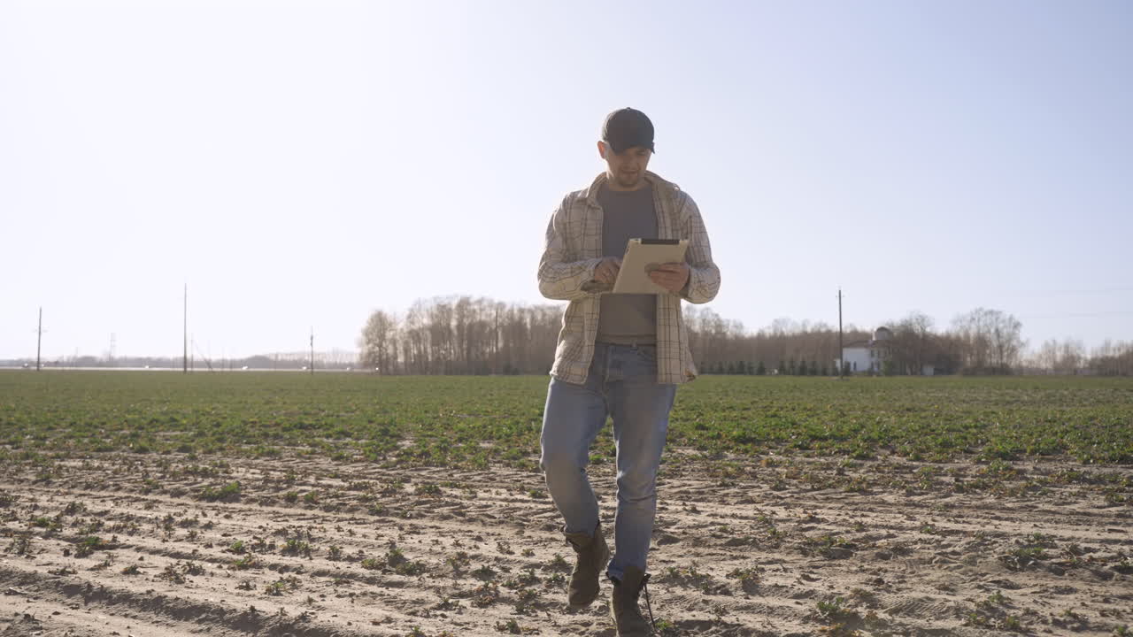 hombre caucásico en camisa a cuadros usando una tableta mientras camina por el campo