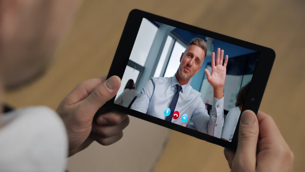 Primo piano di un uomo d'affari che saluta lo schermo di un tablet durante una videochiamata online in ufficio