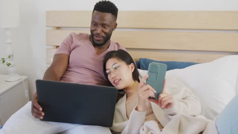 pareja feliz diversa usando computadora portátil y acostada en el dormitorio