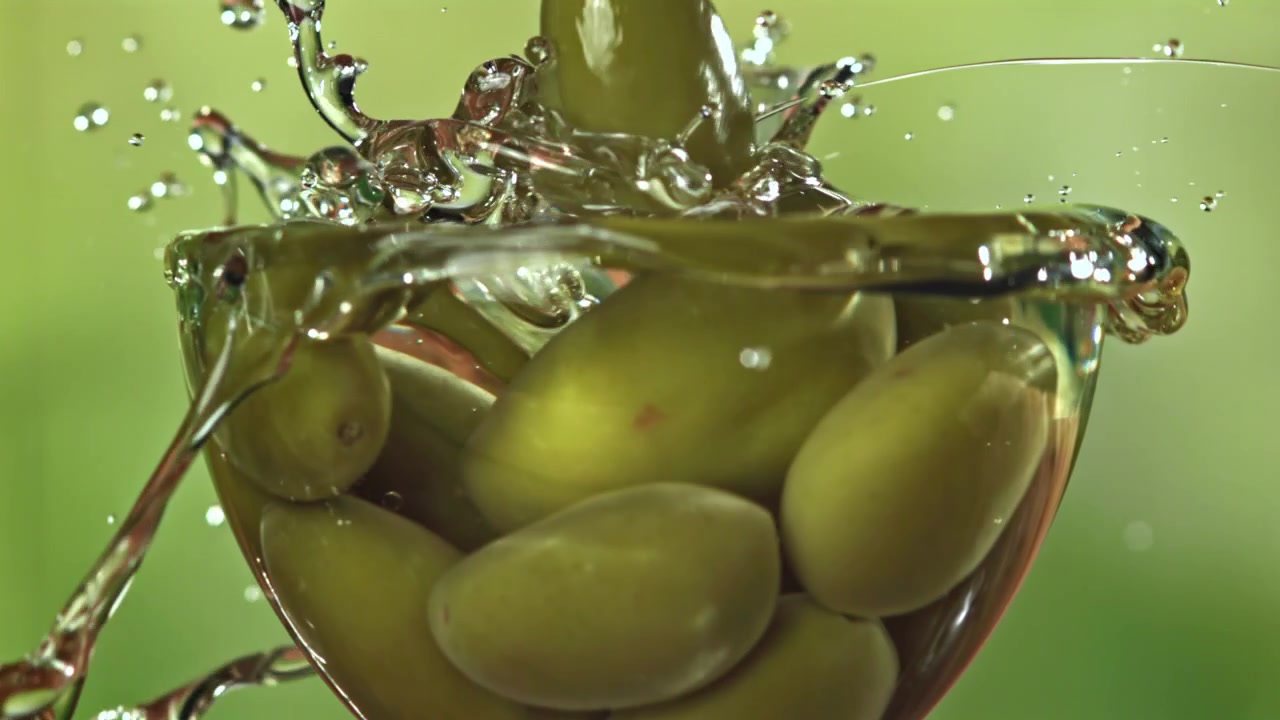 Olive verdi che cadono in un bicchiere con schizzi al rallentatore