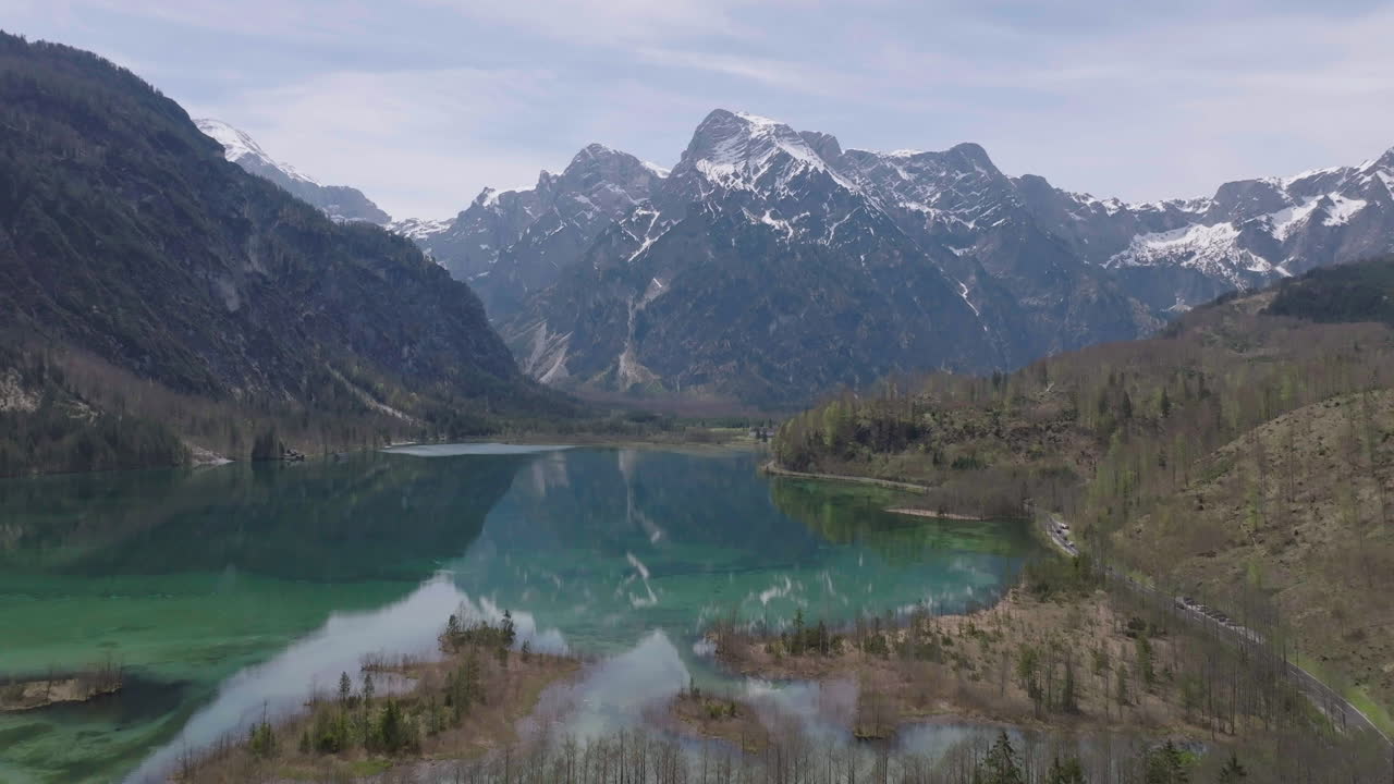 vista aérea de un lago alpino en los alpes austriacos, agua turquesa con reflejo en picos nevados, toma de dron