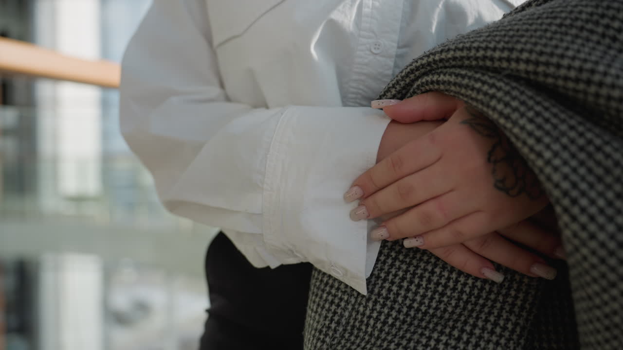 Lady with neatly polished designer fingernails carrying checkered blazer while walking indoors, soft light highlighting detailed fabric texture and subtle hand tattoo in blur modern background