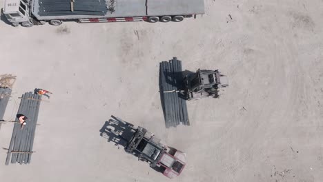 Aerial-top-down-shot-of-forklift-loading-steel-exported-by-cargo-ship-at-port-on-truck