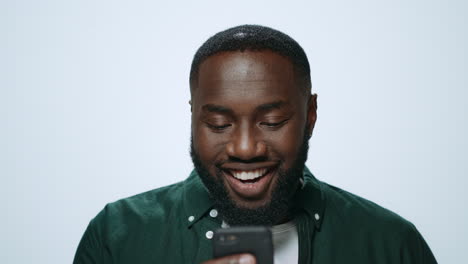 Closeup-happy-african-man-browsing-internet-online-on-mobile-phone-in-studio.