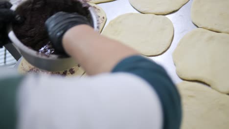 pastry chef hand spreads olive puree atop freshly prepared dough