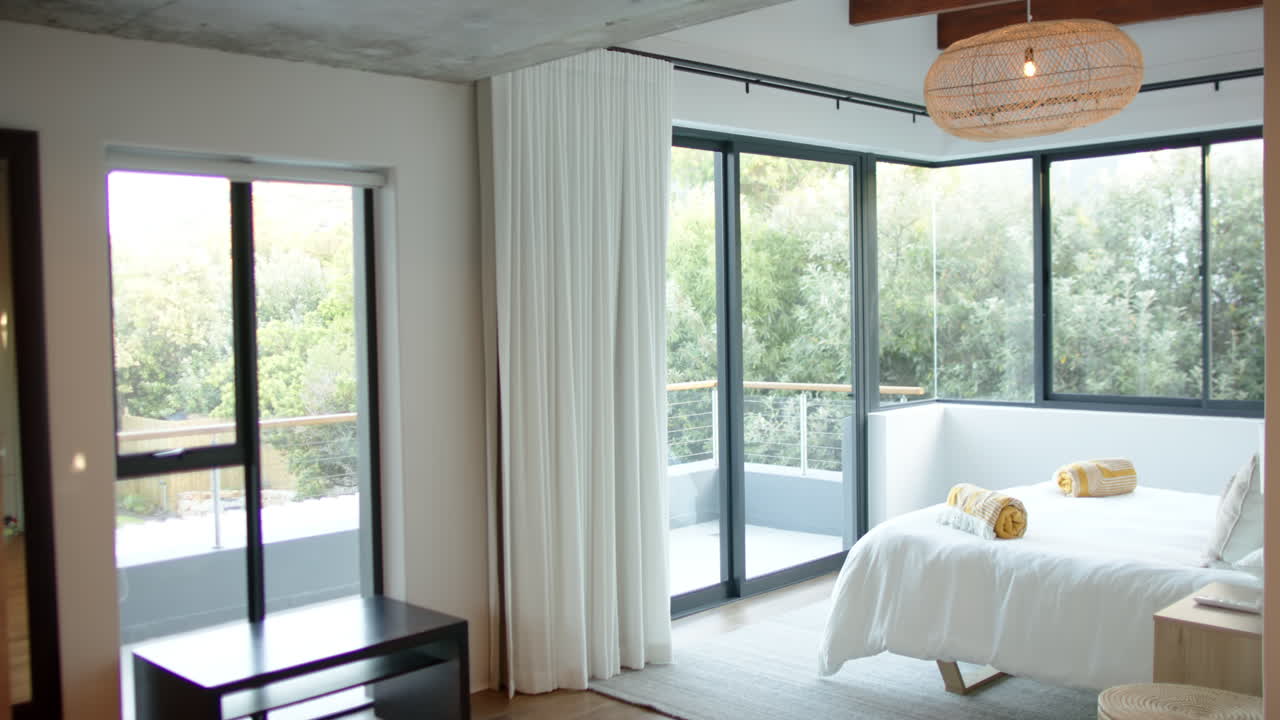 Modern bedroom with large windows, white curtains, and neatly arranged bed linens, copy space