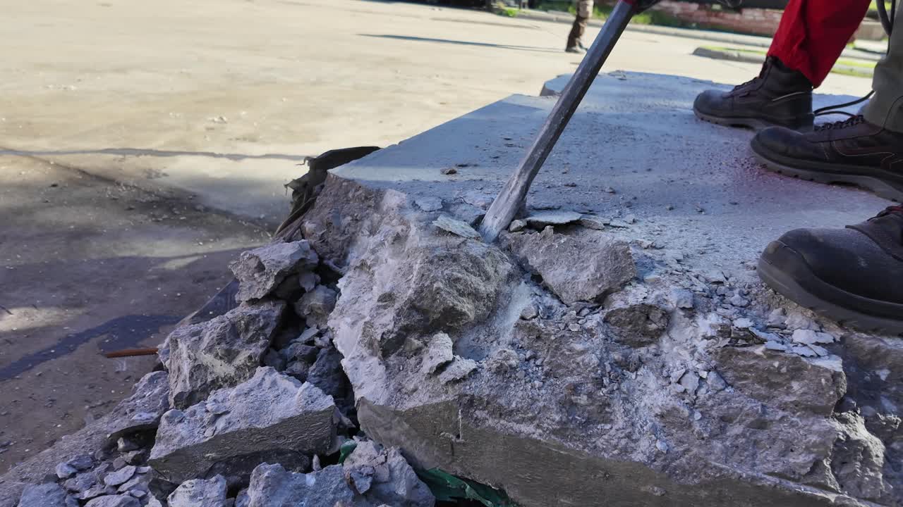 Two men on concrete block, one man using heavy-duty jackhammer tool and breaking reinforced concrete.Concrete fly into pieces in slow motion.