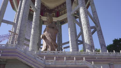 the gigantic statue of kuan yin, goddes of mercy sheltered at the kuan yin pavilion in kek lok si temple in penang malaysia revealed behind the lush tree - low angle shot