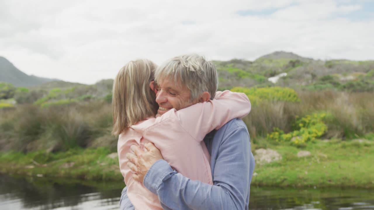 pareja caucásica mayor sonriente abrazándose en el río limpio al aire libre