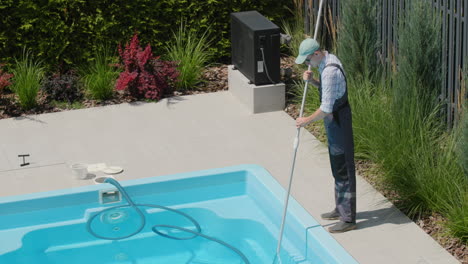 Un-Trabajador-Uniformado-Limpia-La-Piscina-Con-Una-Aspiradora,-Elimina-La-Suciedad-Del-Fondo