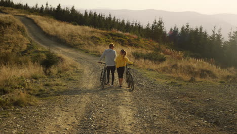 guy and girl having walk with bicycles. bicyclists looking around landscape