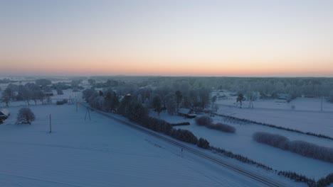 Toma-Aérea-De-Establecimiento-De-Un-Paisaje-Rural,-Casas-De-Campo,-Campos-Agrícolas-Y-árboles-Cubiertos-De-Nieve,-Clima-Frío-Helado,-Resplandor-De-La-Luz-De-La-Hora-Dorada-De-La-Puesta-De-Sol,-Toma-Amplia-De-Drones-Avanzando