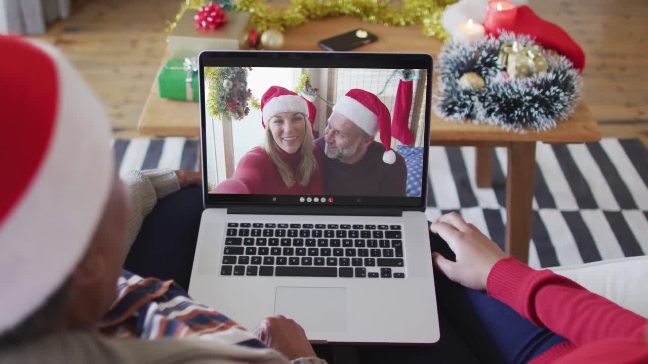 madre y hija afroamericanas usando una computadora portátil para una videollamada de navidad con la pareja en la pantalla